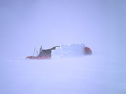 foto preciosa, algo alejada del campamento, en medio de una intenso blizzard o tormenta de viento, que arrastraba mucha nieve, mientras una persona arreglaba algo en el muro. Sin el no duraríamos mucho.